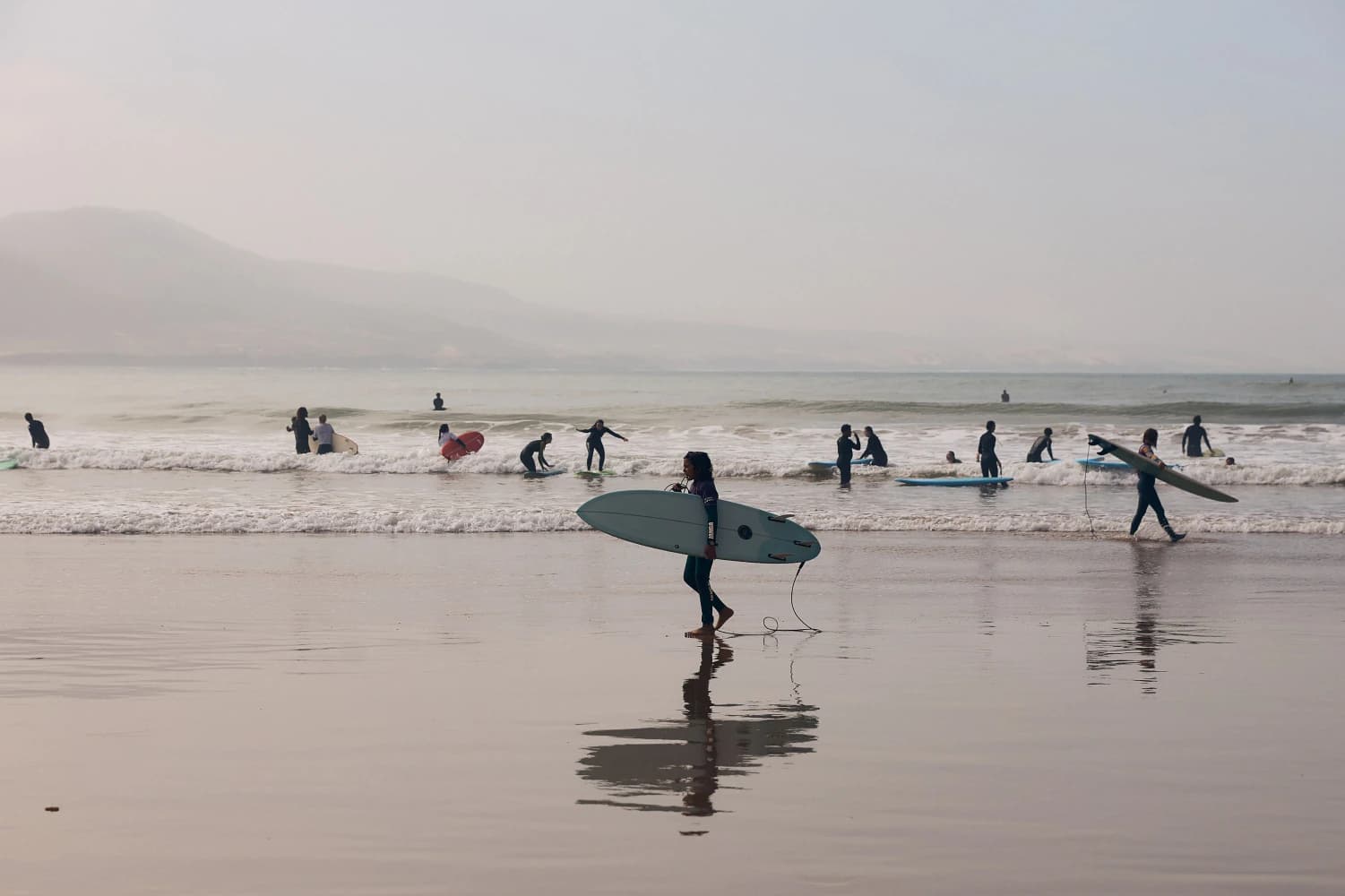 Surfer carrying board across wet sand at Aman Surf & Yoga in Imsouane, Morocco