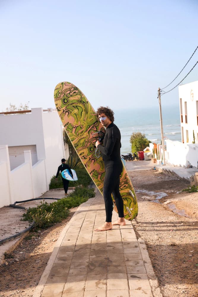 Surfer carrying board through village at Aman Surf & Yoga in Imsouane, Morocco