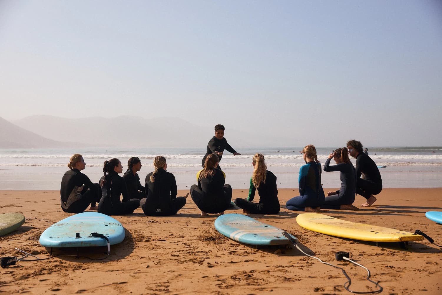 Surfers listening to coach by ocean at Aman Surf & Yoga in Imsouane, Morocco