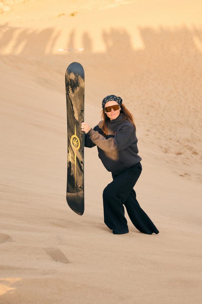 Woman holding sandboard in desert at Aman Surf & Yoga in Imsouane, Morocco