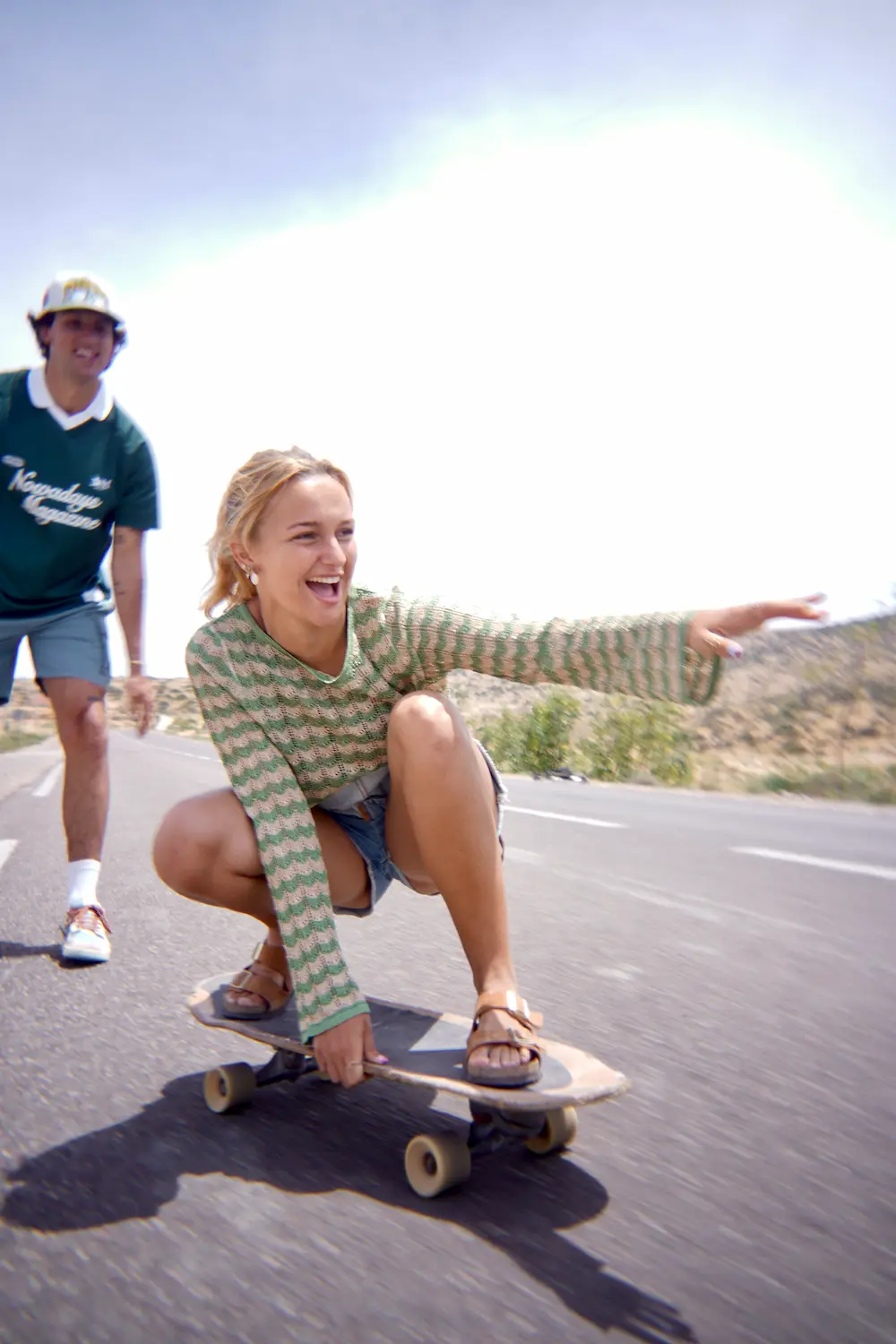 Smiling guest riding low on a surfskate with a coach behind her in Imsouane, Morocco.