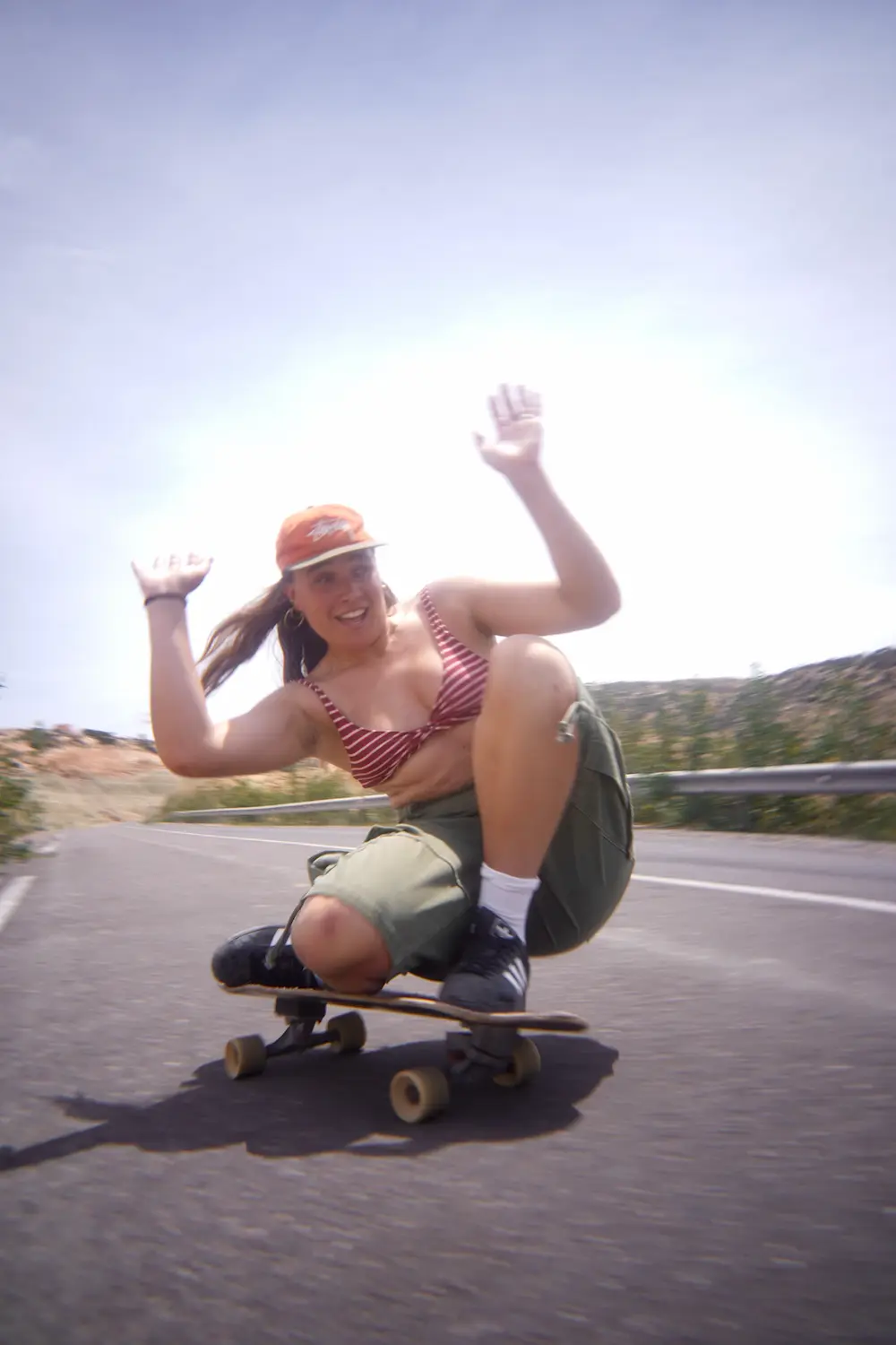 Guest in a red striped top crouching low on a surfskate on a coastal road in Imsouane, Morocco.